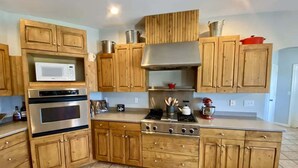 Una cocina con alacenas de madera, microondas, horno, estufa y varios utensilios de cocina.