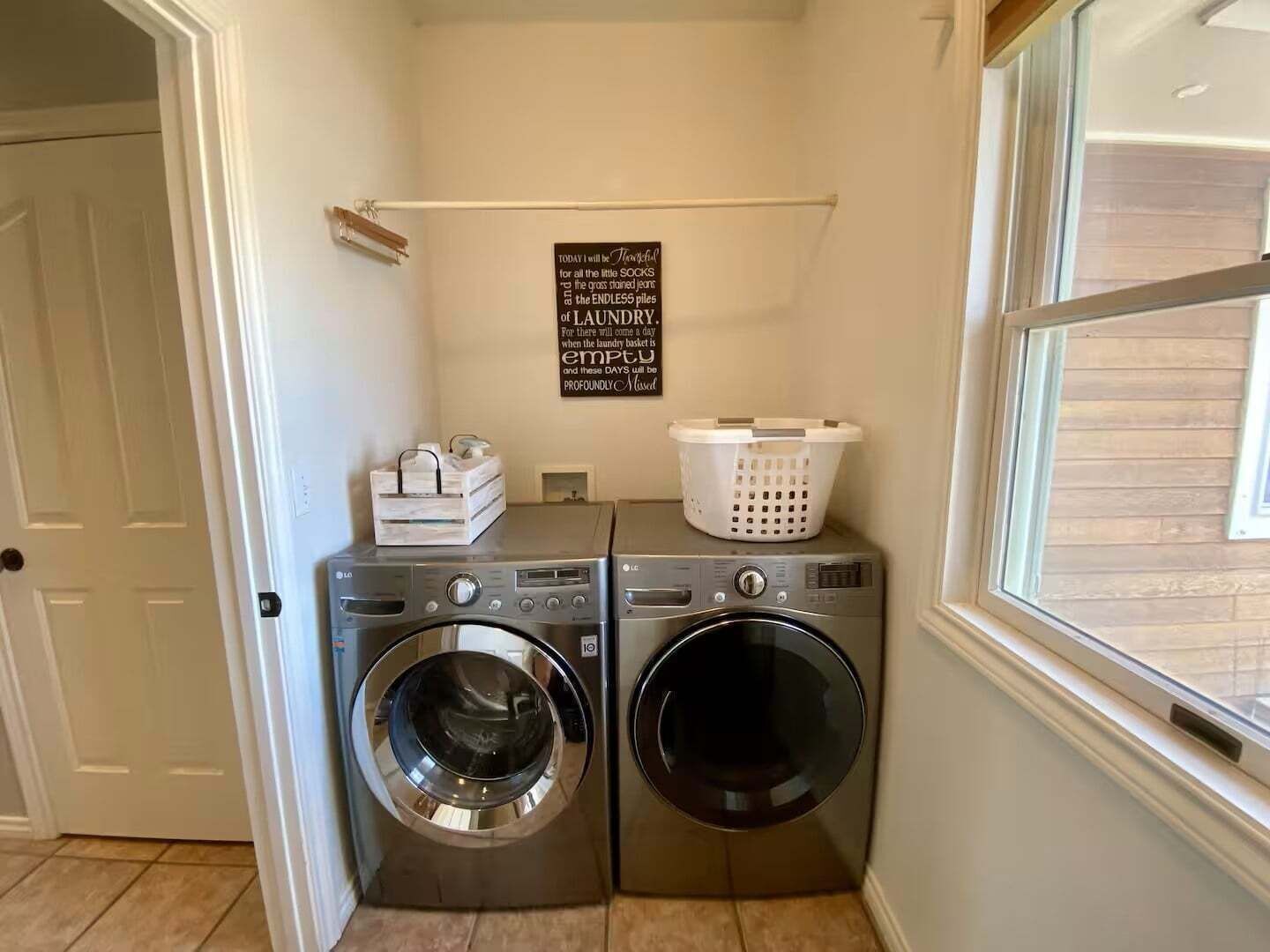 A laundry room with two front-loading washing machines, a drying rack, and a basket on the wall.