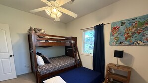 Habitación con literas, ventilador de techo, ventana con cortinas, mapa en la pared y una mesita de noche de madera con lámpara.