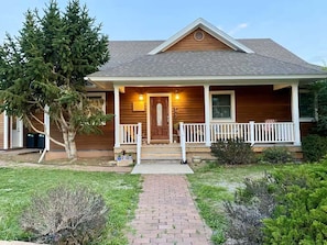 A wooden house with a front porch, a door, and a small garden area. - The Gathering Place 4 Bedroom Home (Montrose)