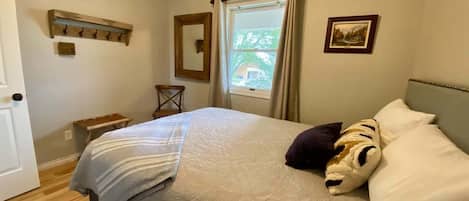 A bedroom with a bed, a window with curtains, a wooden headboard, a wall-mounted picture, and a ceiling fan.