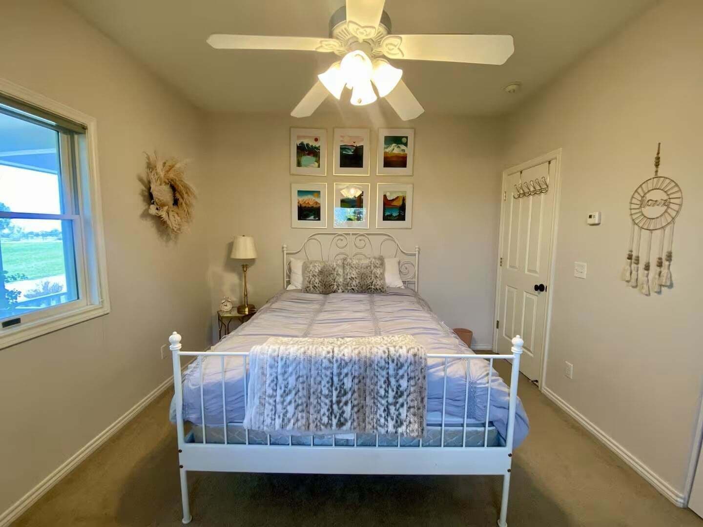 A bedroom with a bed, a ceiling fan, a window, and wall decorations.