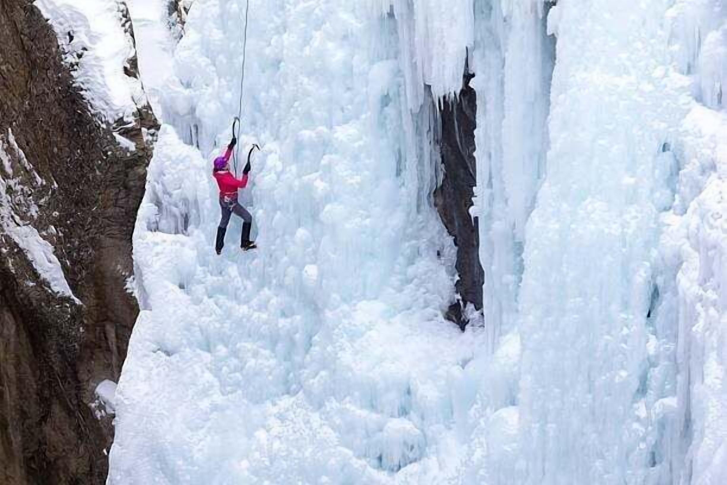 A person ice climbing a vertical ice wall.