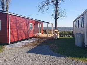 Une cabane rouge avec une terrasse en bois, un chemin de gravier et une vue sur un vignoble.