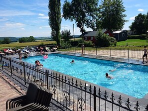 Une piscine où des gens se baignent, une terrasse entourée d’une clôture et une vue sur la campagne.