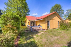 Ein eingeschossiges Holzhaus mit rotem Dach, einer Veranda mit Bank und einer kleinen Terrasse.