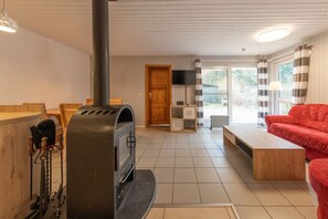 A living room with a fireplace, a red sofa, a wooden bench, and a television. - Skandinavischer Doppelbungalow mit Kaminofen im Ferienpark Mirow (Mirow)