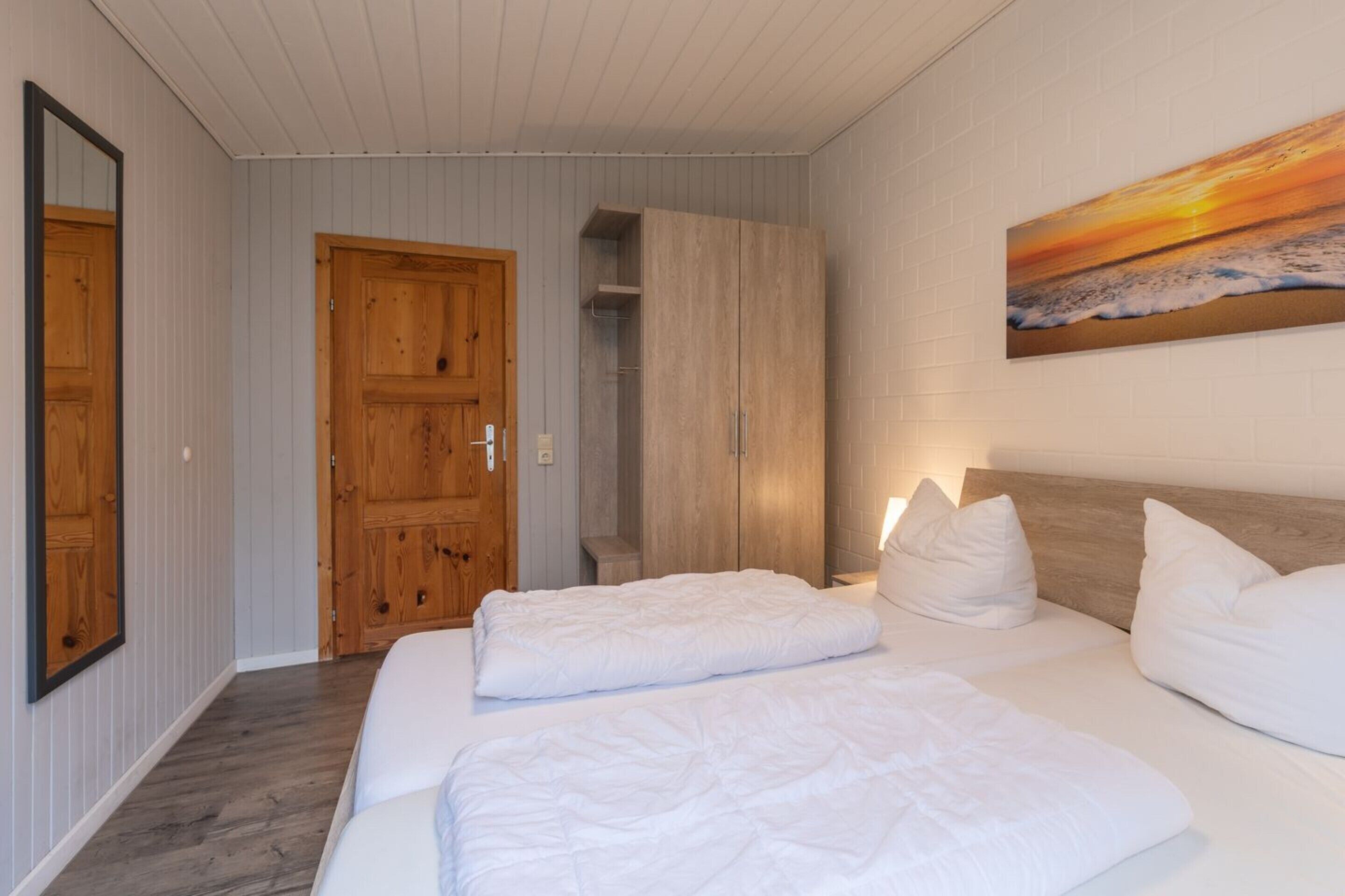 Een hotelkamer met twee bedden, een houten kast, een deur en een schilderij van een ondergaande zon.