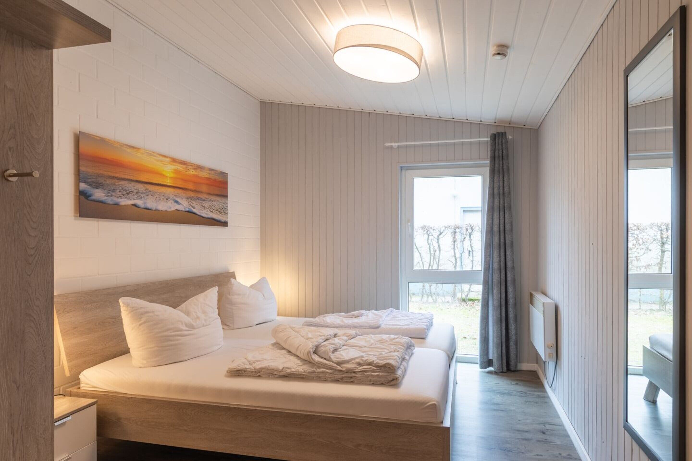 Une chambre à coucher avec un lit, une table de chevet, un tableau, une fenêtre et une vue sur l’extérieur.