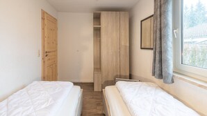 Quarto com duas camas, um guarda-roupa de madeira, um armário e uma janela com cortinas.