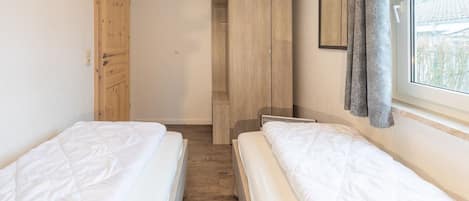 Un dormitorio con dos camas, un armario de madera, un ropero y una ventana con cortinas.
