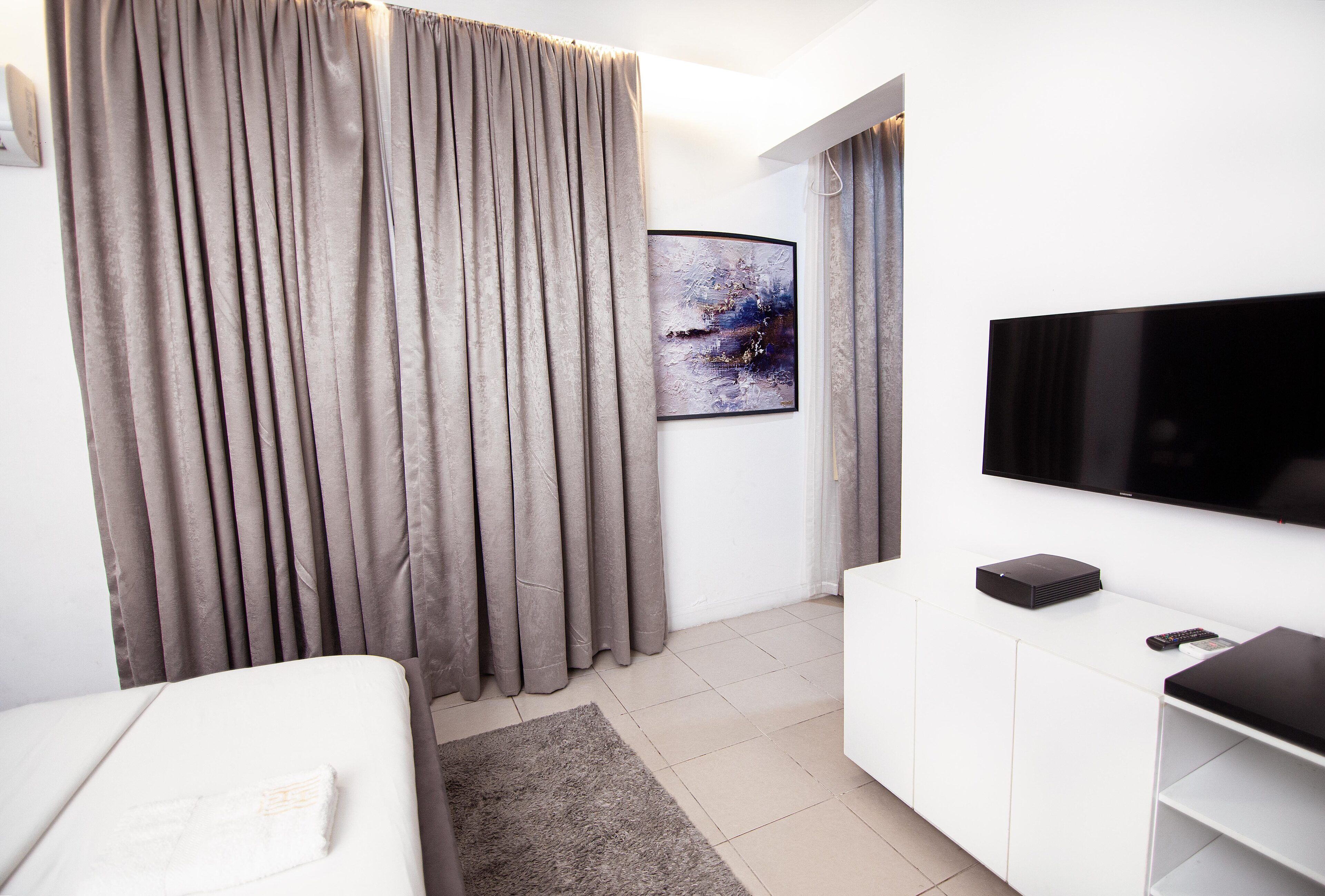 A modern hotel room with a bed, a flat-screen TV, a small cabinet, and a painting on the wall.