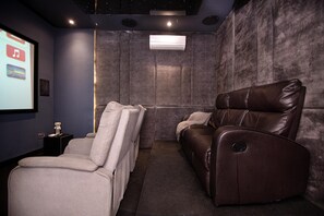 A home theater room with a reclining leather chair, a white armchair, and a small table with a remote control. - DH Cadogan (Lekki)