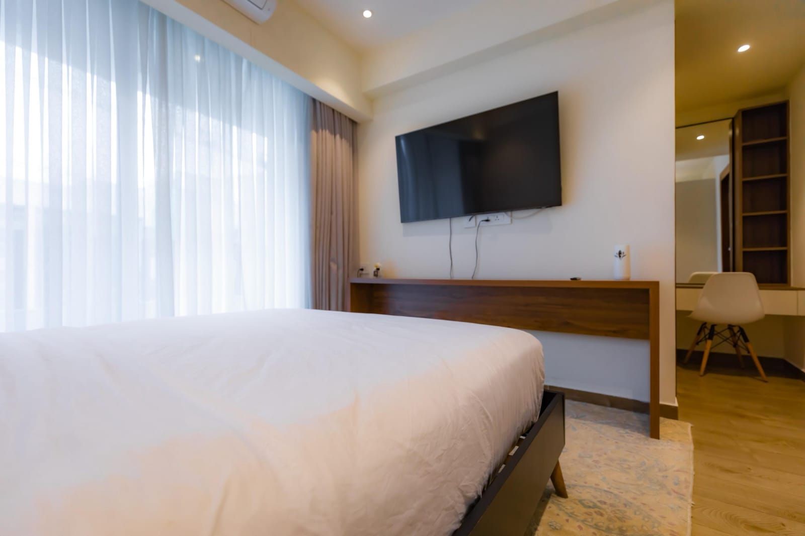 Habitación de hotel con una cama grande, un televisor de pantalla plana montado en la pared y un escritorio con una silla.