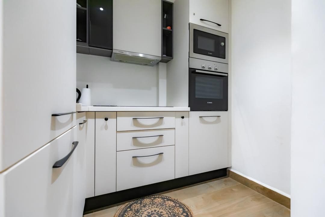Una cocina con armarios blancos, encimera negra y dos hornos.
