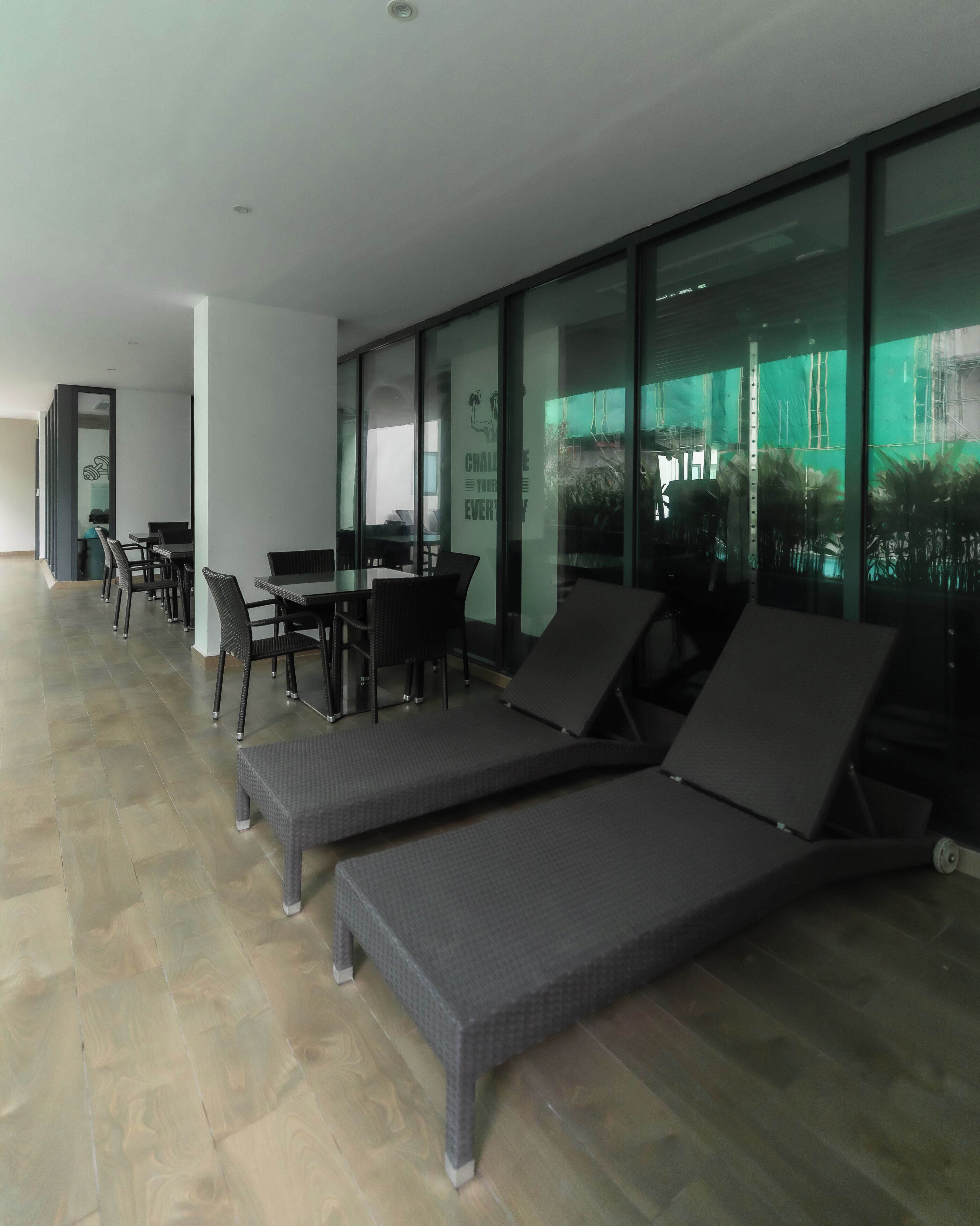 A modern lounge area with seating and a table, large windows, and a view of greenery outside.