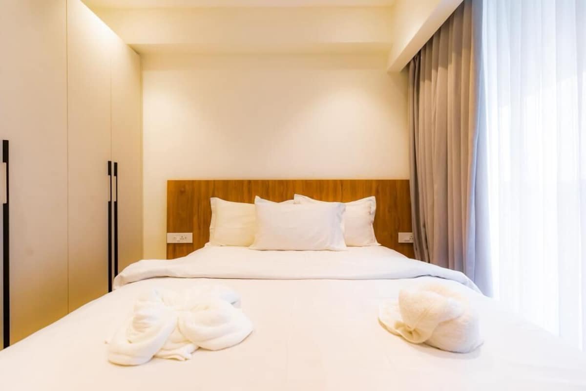 Ein Hotelzimmer mit einem Bett, Kissen, einem Holzkopfende und einem Fenster mit Vorhängen.