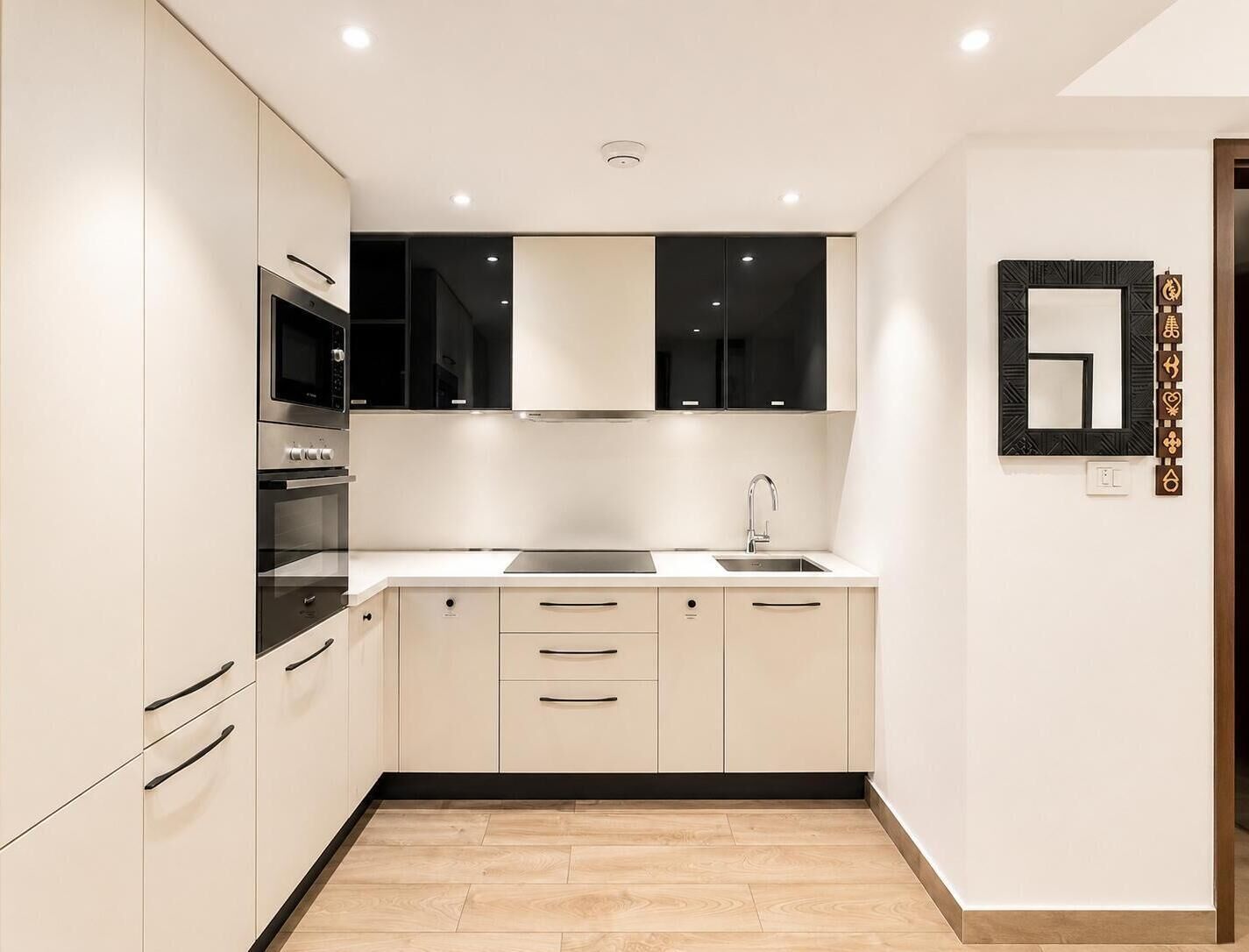 Una cocina moderna con armarios blancos, salpicadero negro y un lavamanos de acero inoxidable.