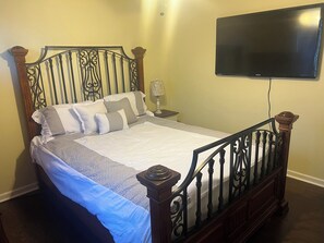 Une chambre à coucher comprenant un lit, une table de chevet, une lampe et un téléviseur fixé au mur.