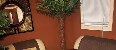 A living room with a sofa, armchairs, a coffee table, a decorative plant, and a wall-mounted mirror.