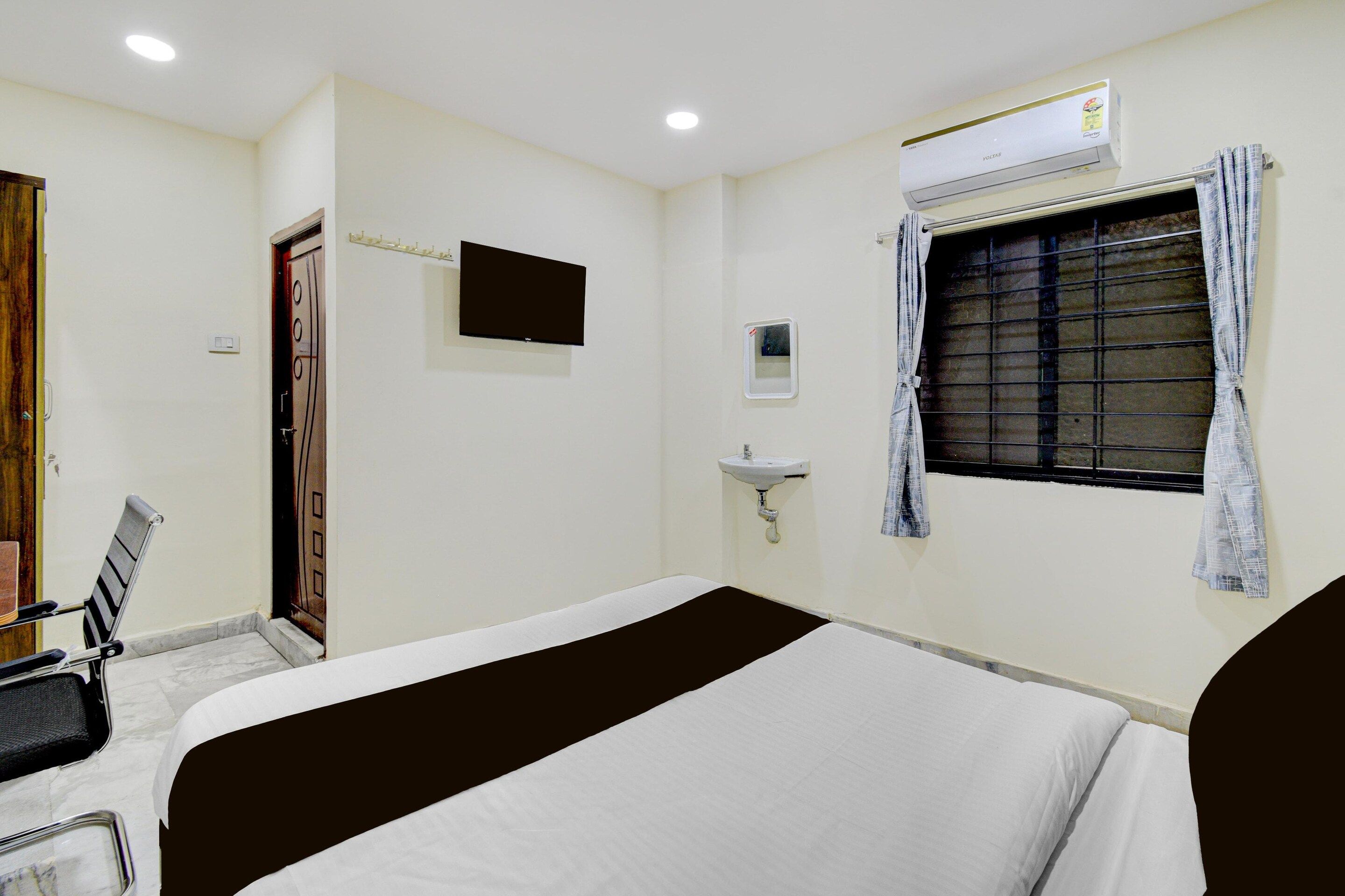 A hotel room with a bed, a television, a window with curtains, a sink, and an air conditioning unit.