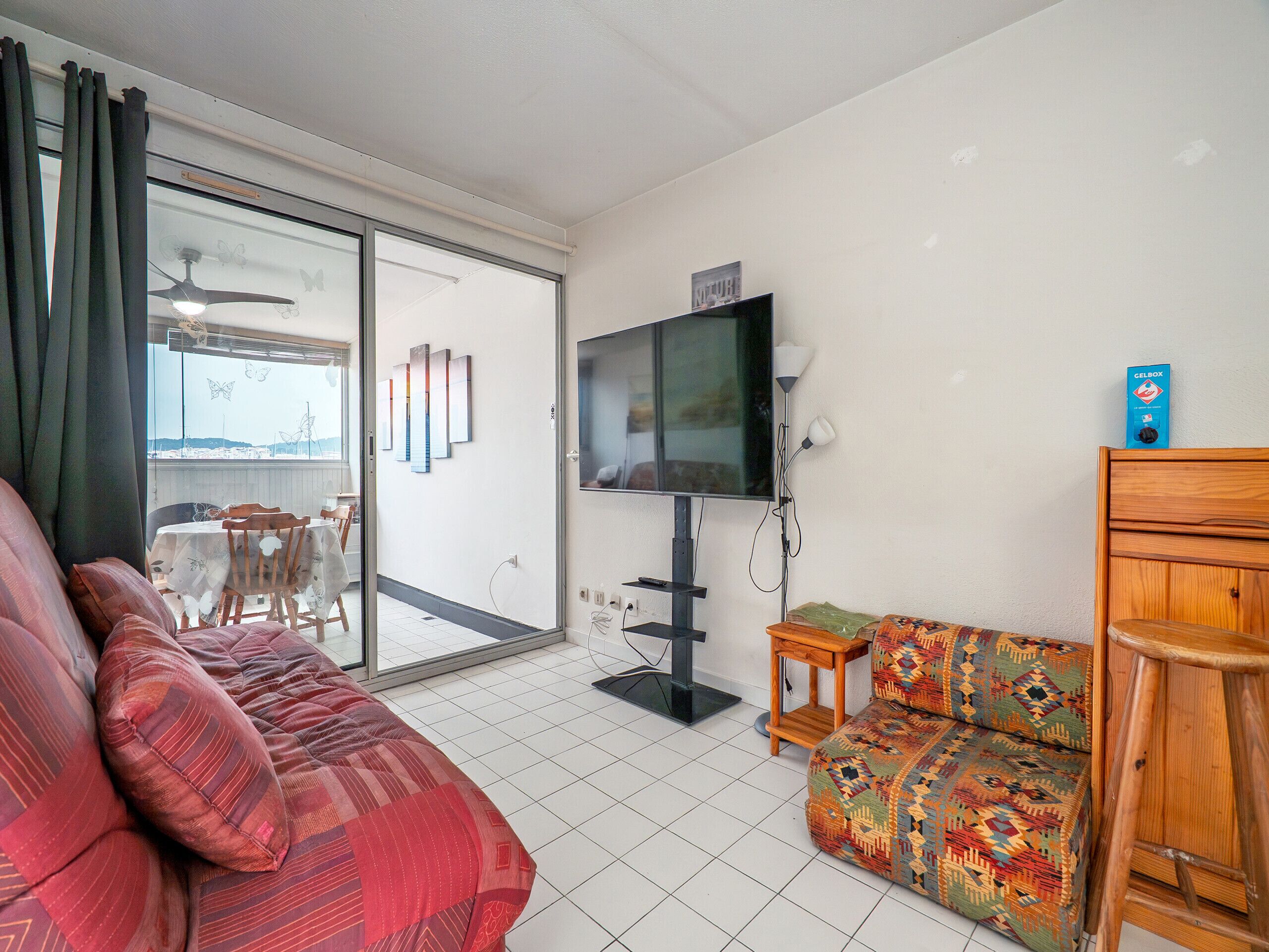 A living room with a sofa, a patterned ottoman, a television, and a ceiling fan.