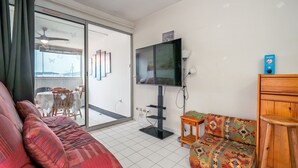Un soggiorno con un divano, un poggiapiedi decorato, una televisione e una ventola a soffitto.