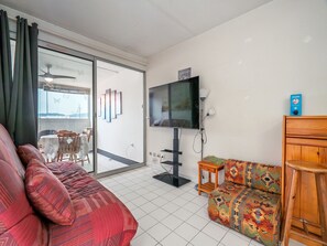 Ein Wohnzimmer mit einer Couch, einem gemusterten Hocker, einem Fernseher und einem Deckenventilator.