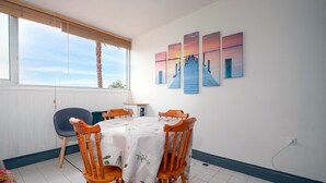 Zona pranzo con tavolo imbandito per quattro, sedie in legno, una finestra con persiane e parete con tre quadri.