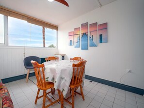 Ein Essbereich mit einem Tisch für vier Personen, Holzsesseln, einem Fenster mit Jalousien und einer Wand mit drei Bildern.