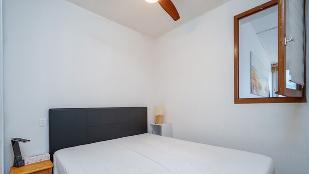 Una camera da letto con un letto, un comodino, una lampada e una ventola a soffitto.