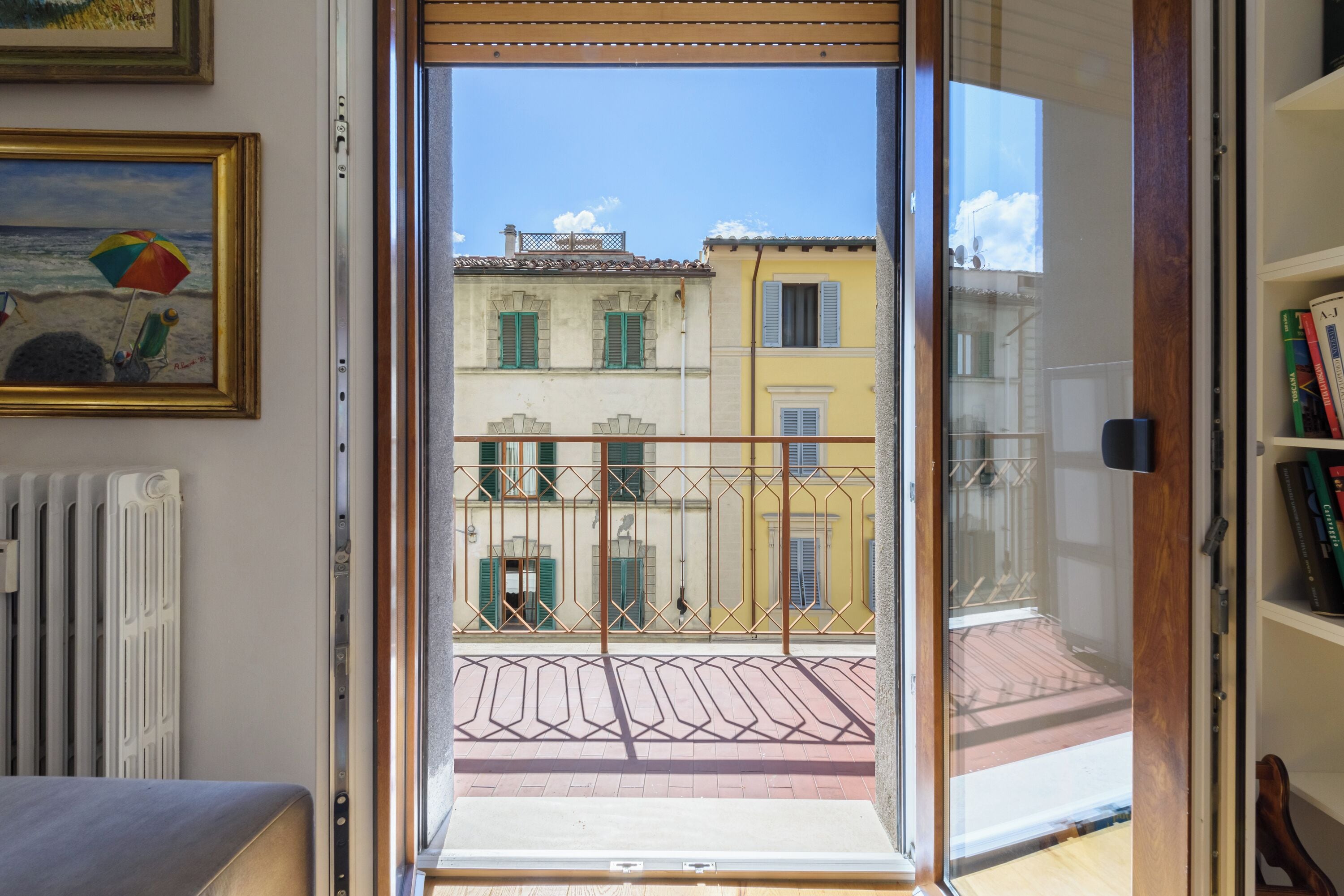 A room with a view of a building with balconies, a radiator, and a bookshelf.