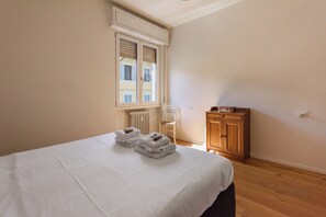 Una habitación de hotel con una cama, un armario de madera, una silla y una ventana con contraventanas.