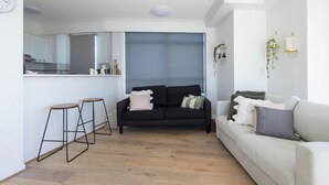A modern living room with a black sofa, a white sofa, and a wooden floor. - Breezy 2BDR Beachfront Apt in Burleigh Heads (Burleigh Heads)