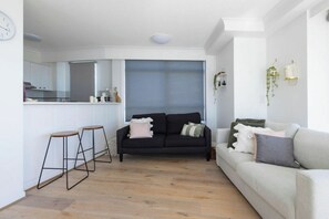 A modern living room with a black sofa, a white sofa, and a wooden floor. - Breezy 2BDR Beachfront Apt in Burleigh Heads (Burleigh Heads)