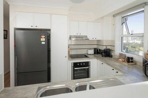 A modern kitchen with a built-in oven, a stovetop, and a refrigerator. - Breezy 2BDR Beachfront Apt in Burleigh Heads (Burleigh Heads)