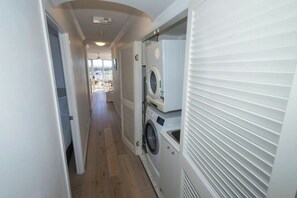 A laundry room with stacked washers and dryers, a wooden floor, and a view of the outside through a door. - Breezy 2BDR Beachfront Apt in Burleigh Heads (Burleigh Heads)