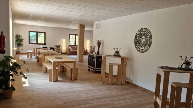 A spacious room with wooden flooring, a fire extinguisher, a potted plant, and a wall-mounted emblem. - Jentilbaratze: More Than Just a Country House. Multifunctional space surrounded by nature (Orozko)