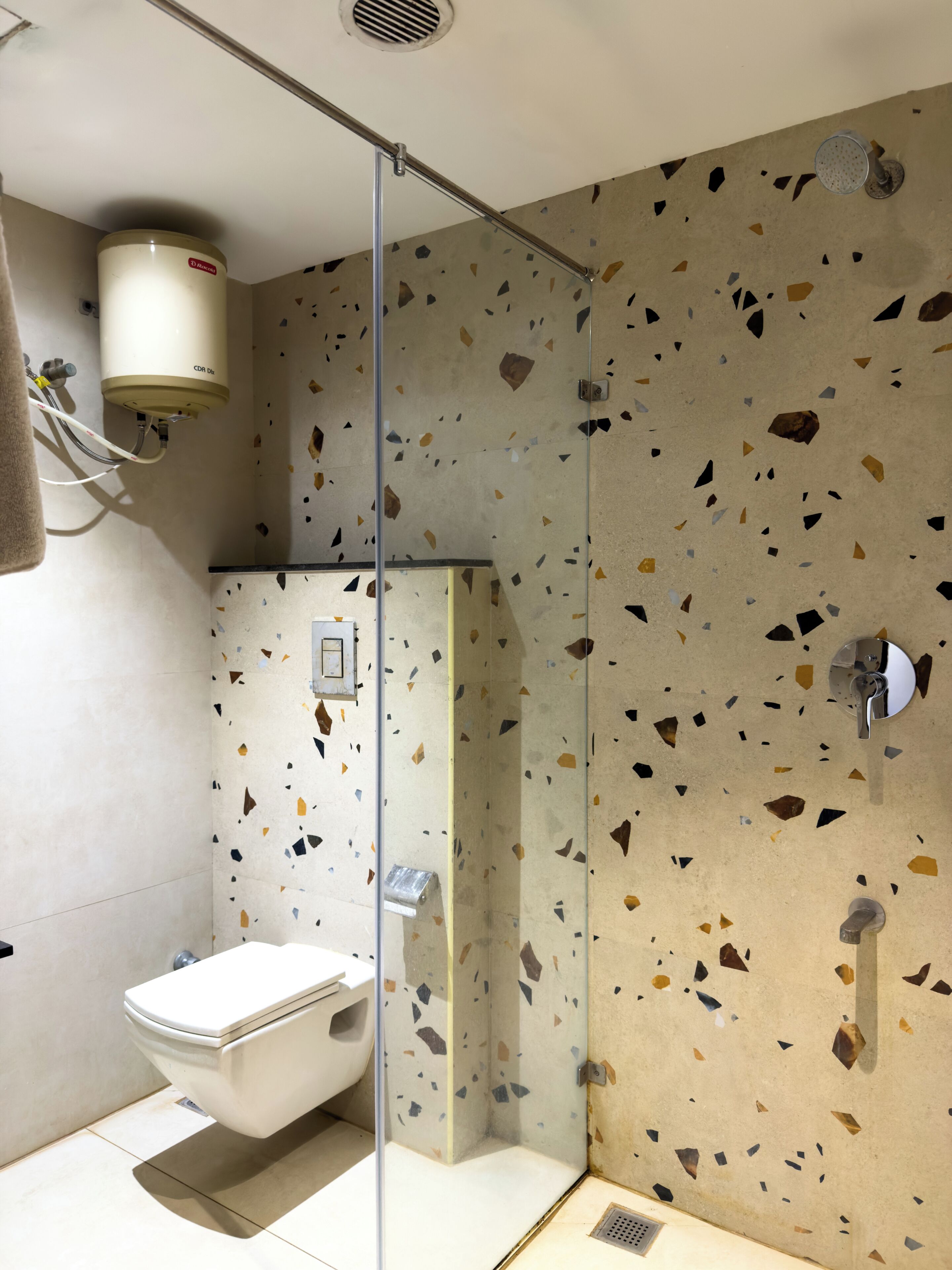 Ein modernes Badezimmer mit einer gläsernen Duschkabine, einer Toilette und einem an der Wand montierten Warmwasserbereiter.