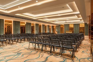 Un salón de conferencias con filas de sillas, una alfombra estampada y un diseño moderno en el techo.