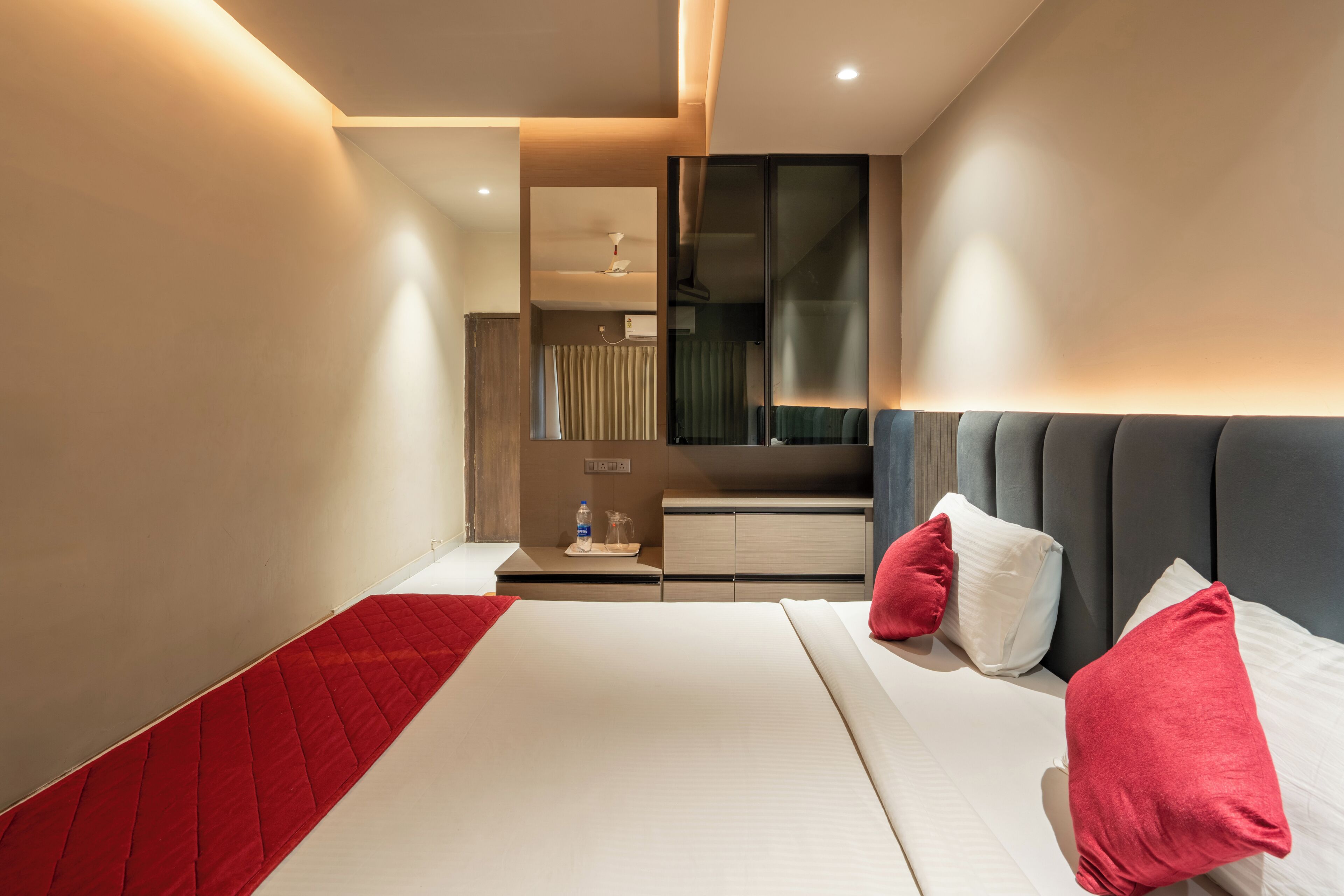A modern hotel room with a bed, bedside tables, a TV, and a minibar.