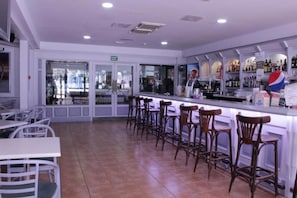 A bar area with a counter, stools, and a view of the street through glass doors. - Hotel Green Field (San Bartolomé de Tirajana)