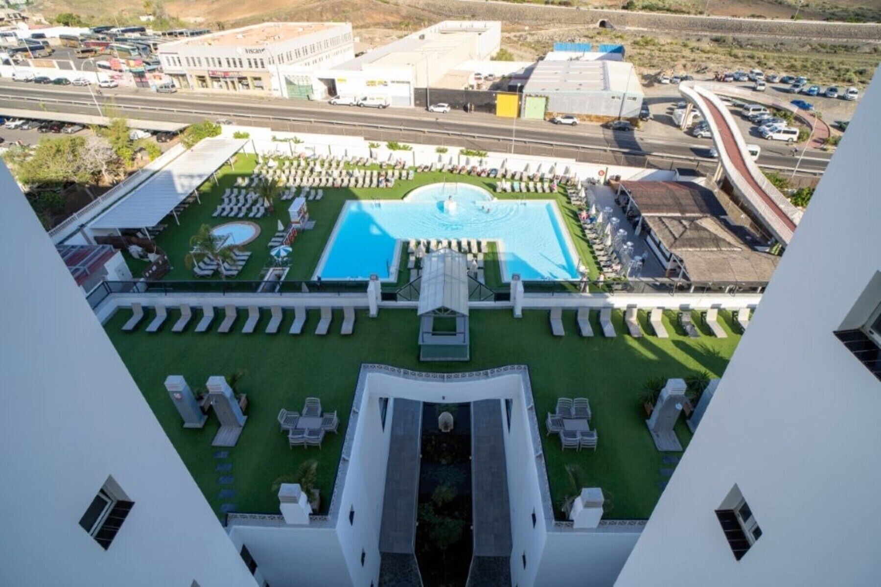 A hotel with a central swimming pool, a landscaped garden, and a view of the surrounding area.
