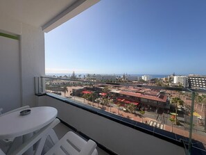 A balcony with a table and chairs, overlooking a cityscape with buildings and a clear sky. - Hotel Green Field (San Bartolomé de Tirajana)