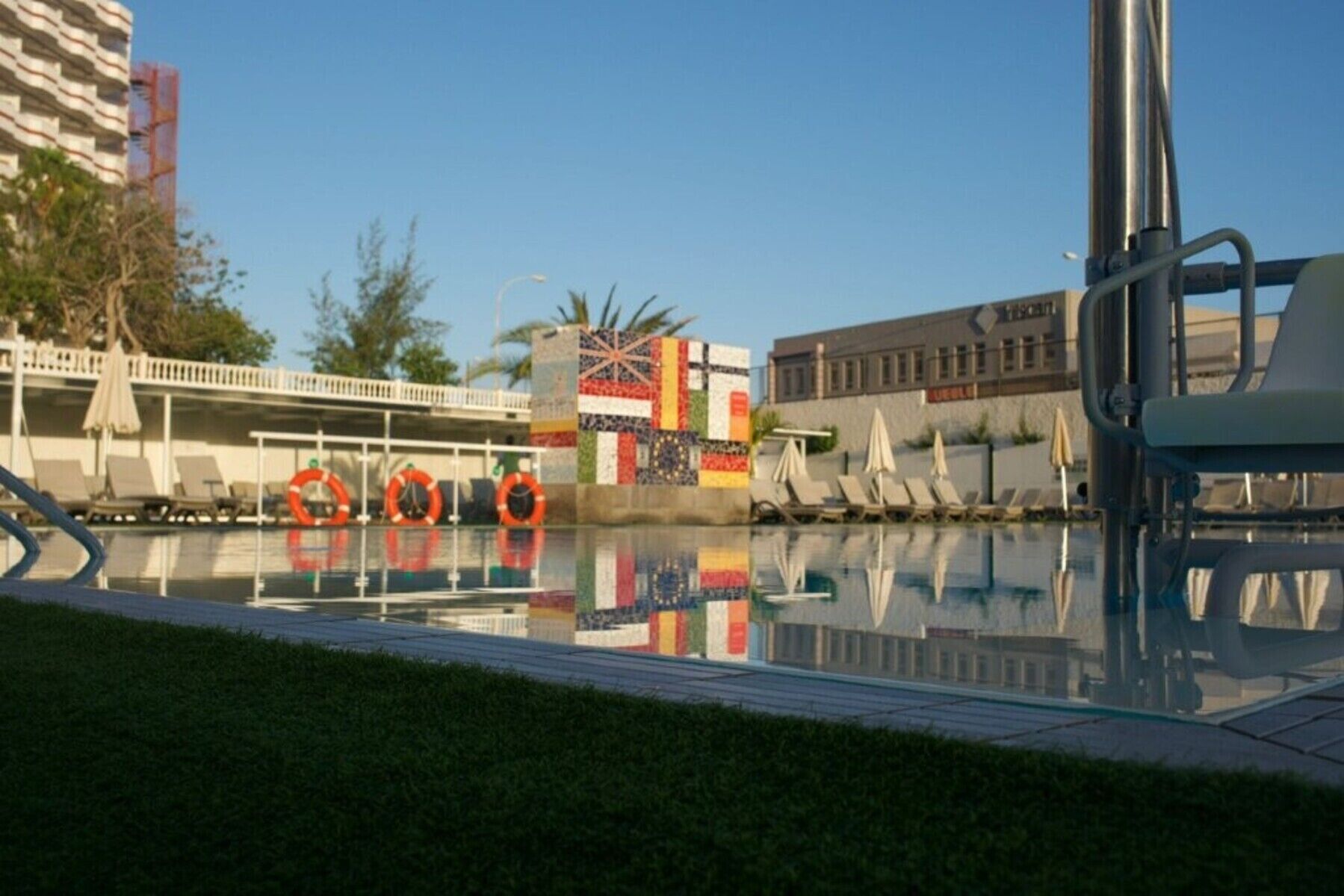 Une piscine avec des chaises longues et des bouées de sauvetage, un pont et un bâtiment avec une enseigne.