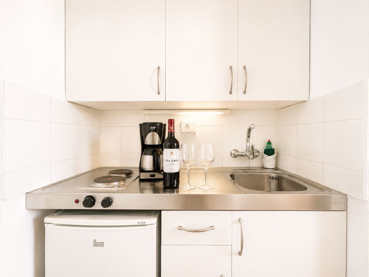 A kitchenette with a coffee maker, wine bottle, glasses, and a dishwasher.