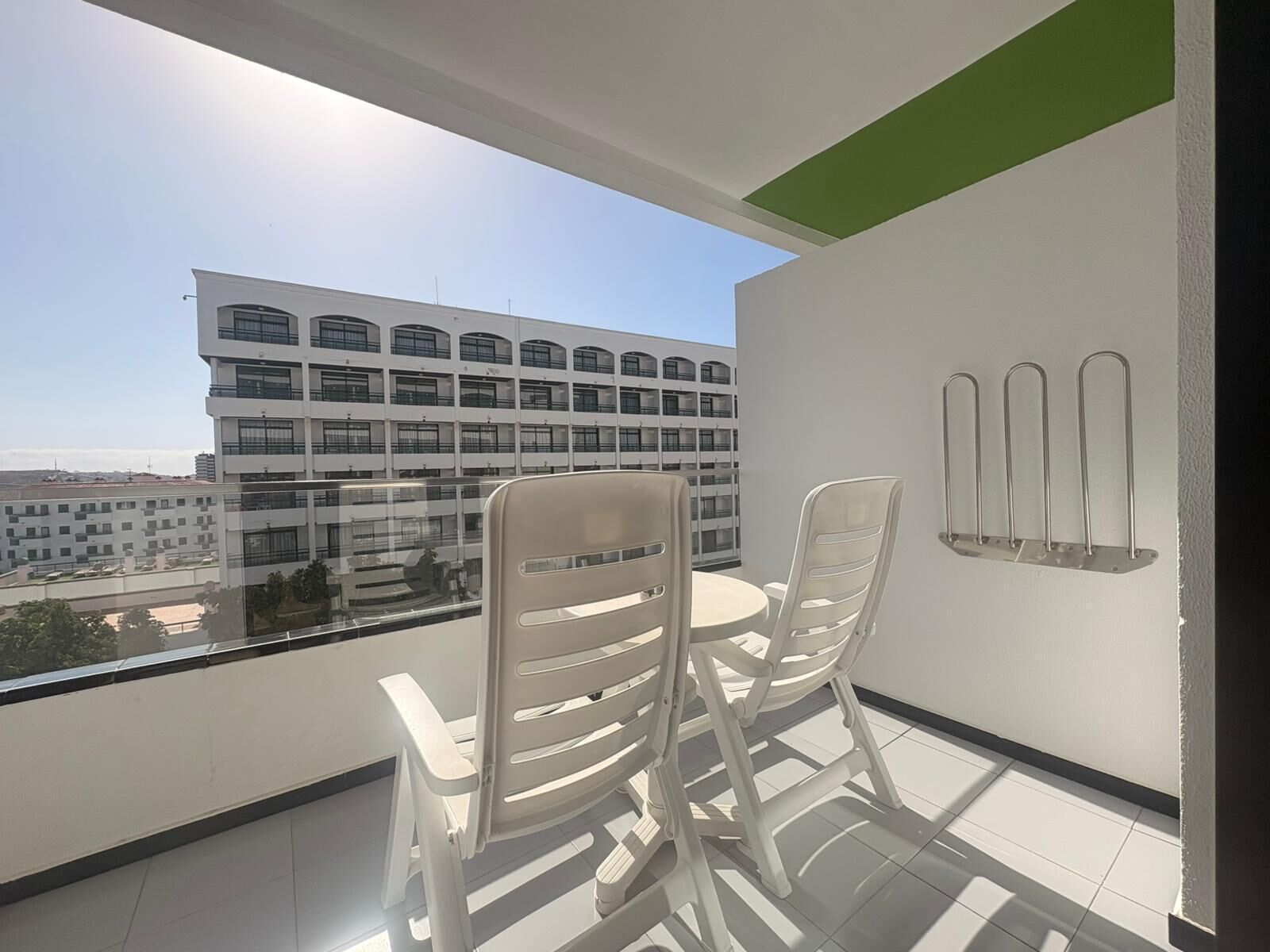 Un balcon avec deux chaises et une table, une vue sur un immeuble à plusieurs étages et un luminaire fixé au mur.