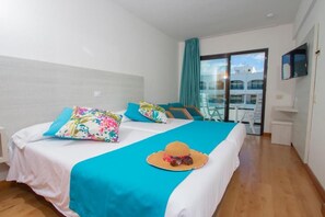A hotel room with a bed, a TV, and a balcony with a view of buildings. - Hotel Green Field (San Bartolomé de Tirajana)