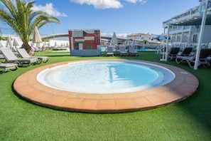 Ein Schwimmbecken mit einer gefliesten Kante, umgeben von künstlichem Gras und Liegestühlen.