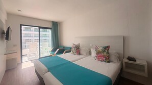 Een hotelkamer met een groot bed, een nachtkastje, een stoel, uitzicht op het balkon en een aan de muur bevestigde televisie.